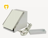 نمای نزدیک از تکنسین لابراتوار در حال تریم کردن الگوی مومی پروتز دندانی با دستگاه تریمر.